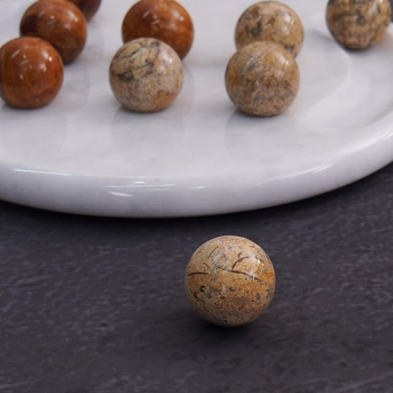 Close-up view of single beige marble ball in front of marble board game – tabletop strategy concept