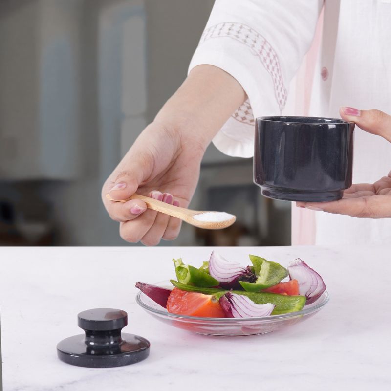 Woman using polished black salt cellar with spoon for seasoning