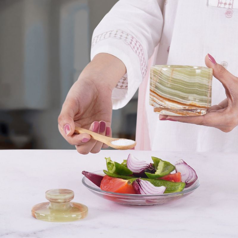 Woman using green onyx marble salt cellar to season salad
