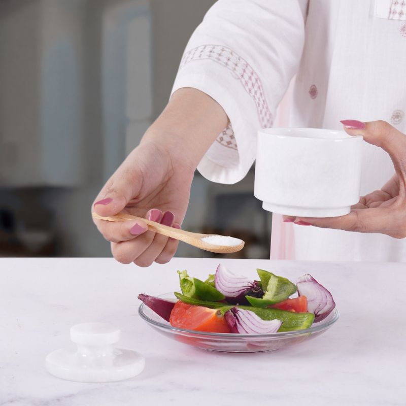 Woman using marble salt cellar with lid and spoon for seasoning salad