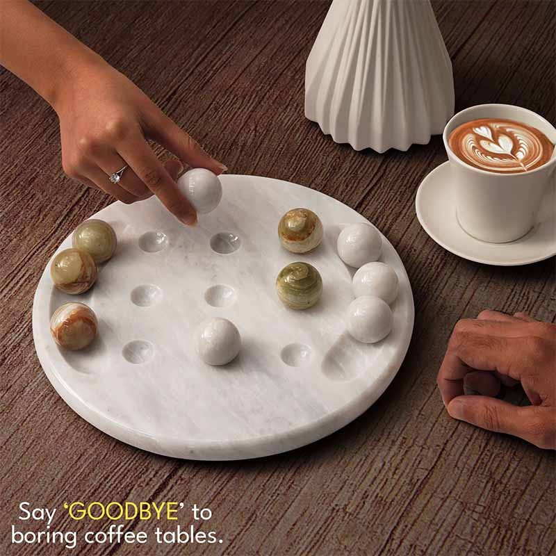 Lifestyle shot of marble tic tac toe board on coffee table with white and green balls, hand placing a marble piece