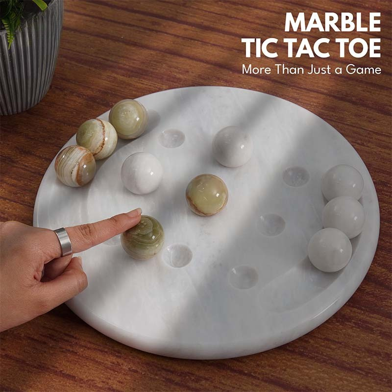 Hand placing green and white marble balls on 10-inch round Tic Tac Toe board game for coffee table use.