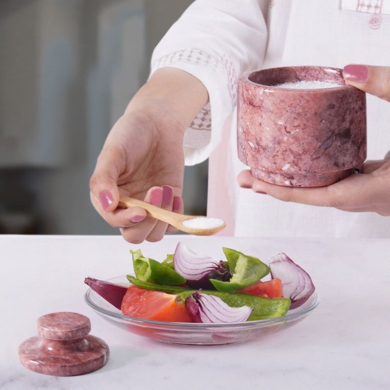 Woman using red marble salt cellar with spoon to season salad